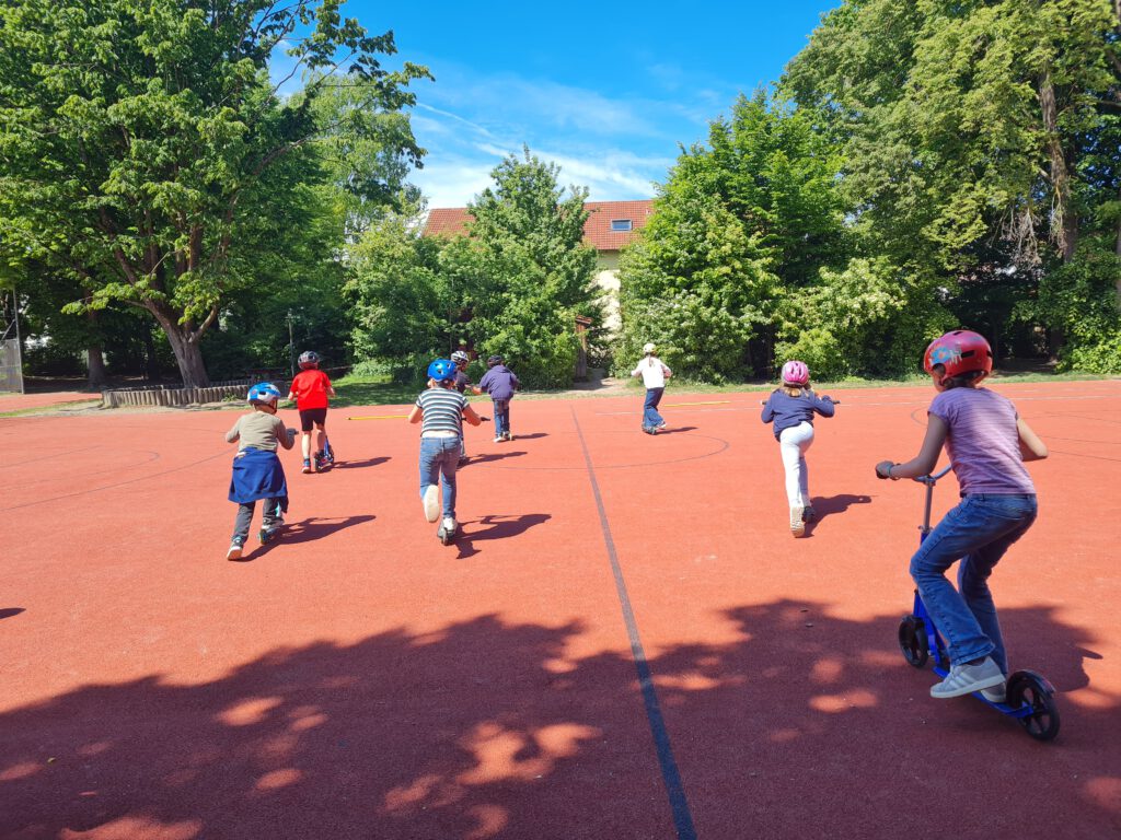 Kinder fahren auf dem Basketballplatz mit den Rollern, alle tragen Helme