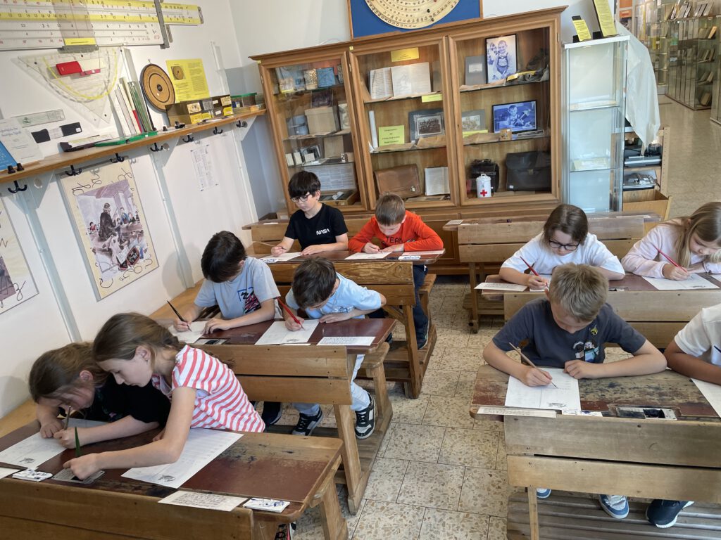 Kinder sitzen an Bänken und arbeiten im antiquen Klassenzimmer
