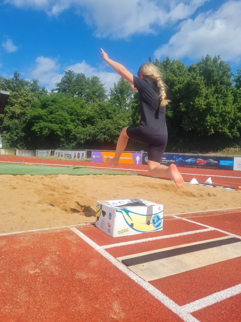 Ein Mädchen springt über einen Karton in die Sprunggrube