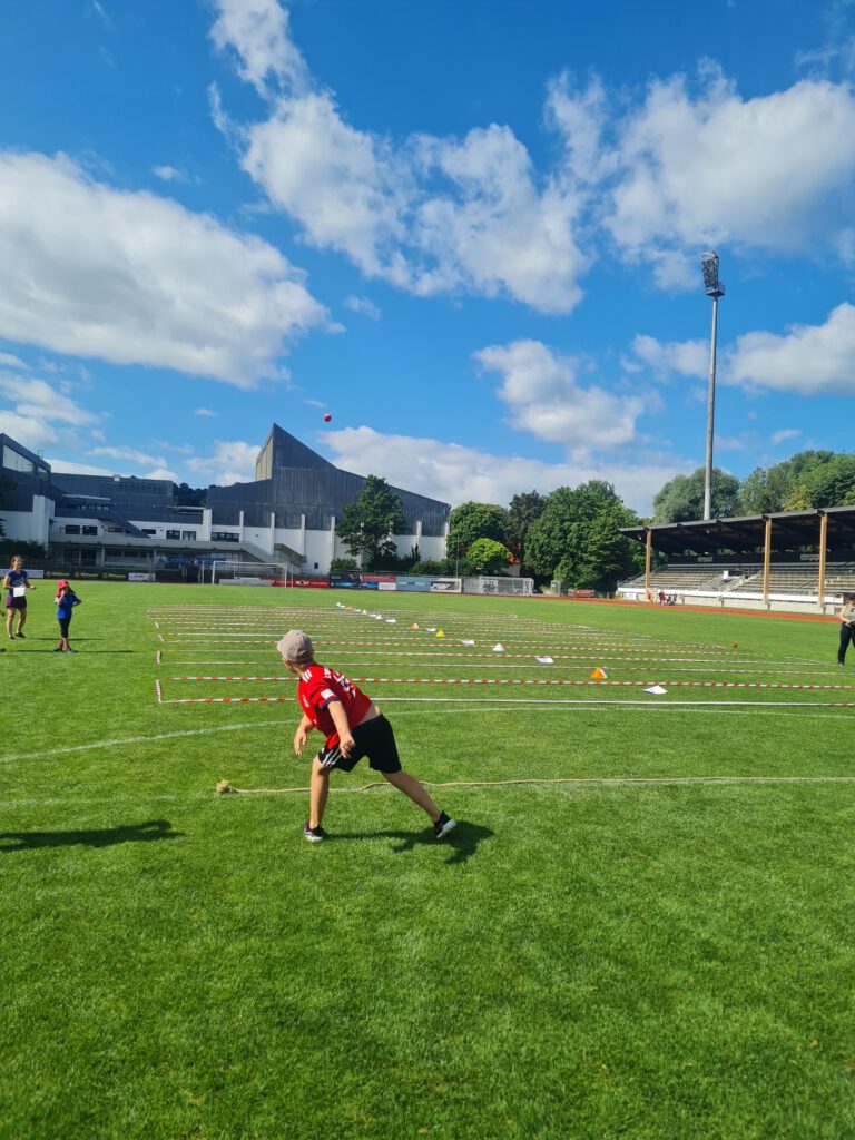 Ein Junge steht an der Abwurflinie und wirft den Schlagball weit nach vorne