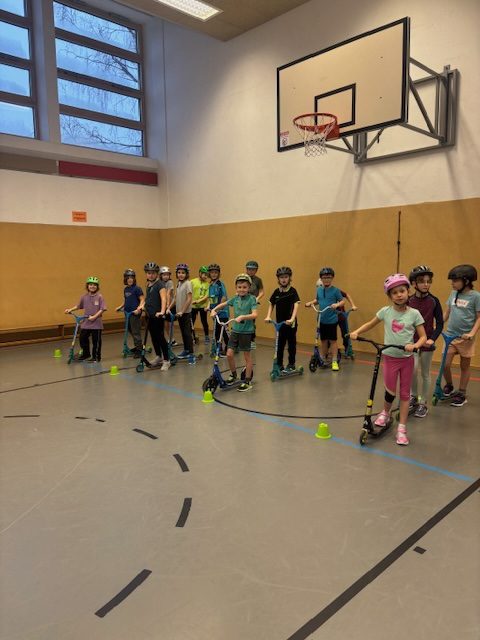 Kinder stehen wartend auf Rollern mit Helmen an und warten auf die nächste Übung