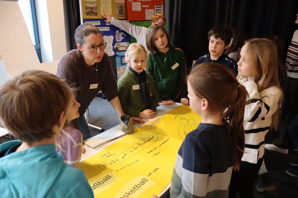 Frau Ringert steht an einem Tisch umringt von SchülerInnen und bespricht ein Plakat.