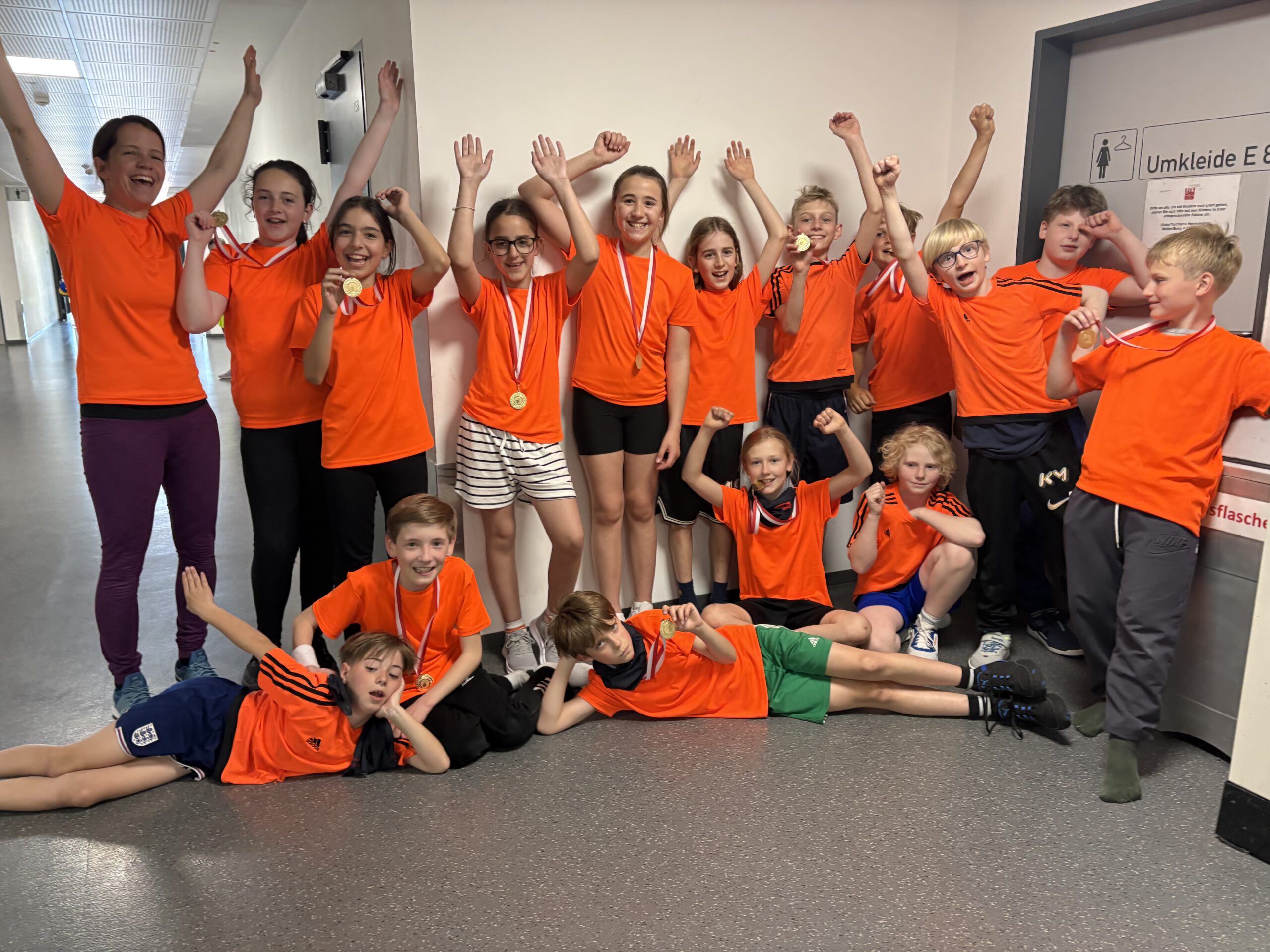 Die Kinder der Mannschaft posen in orangen Trikots jubelnd für ein Bild. Sie haben eine Medaille um den Hals.