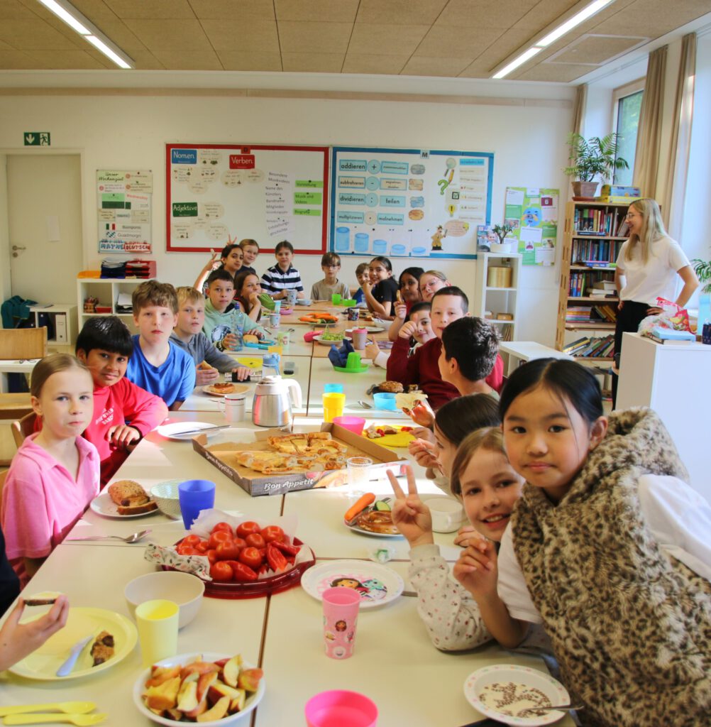 Kinder sitzen an der reich gedeckten Frühstückstafel im Klassenzimmer