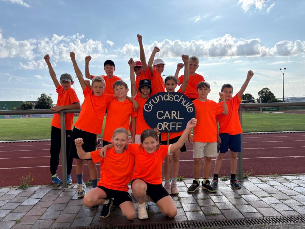 Teilnehmer des Leichtathletikteams stehen in Trikots jubelnd zum Mannschaftsfoto